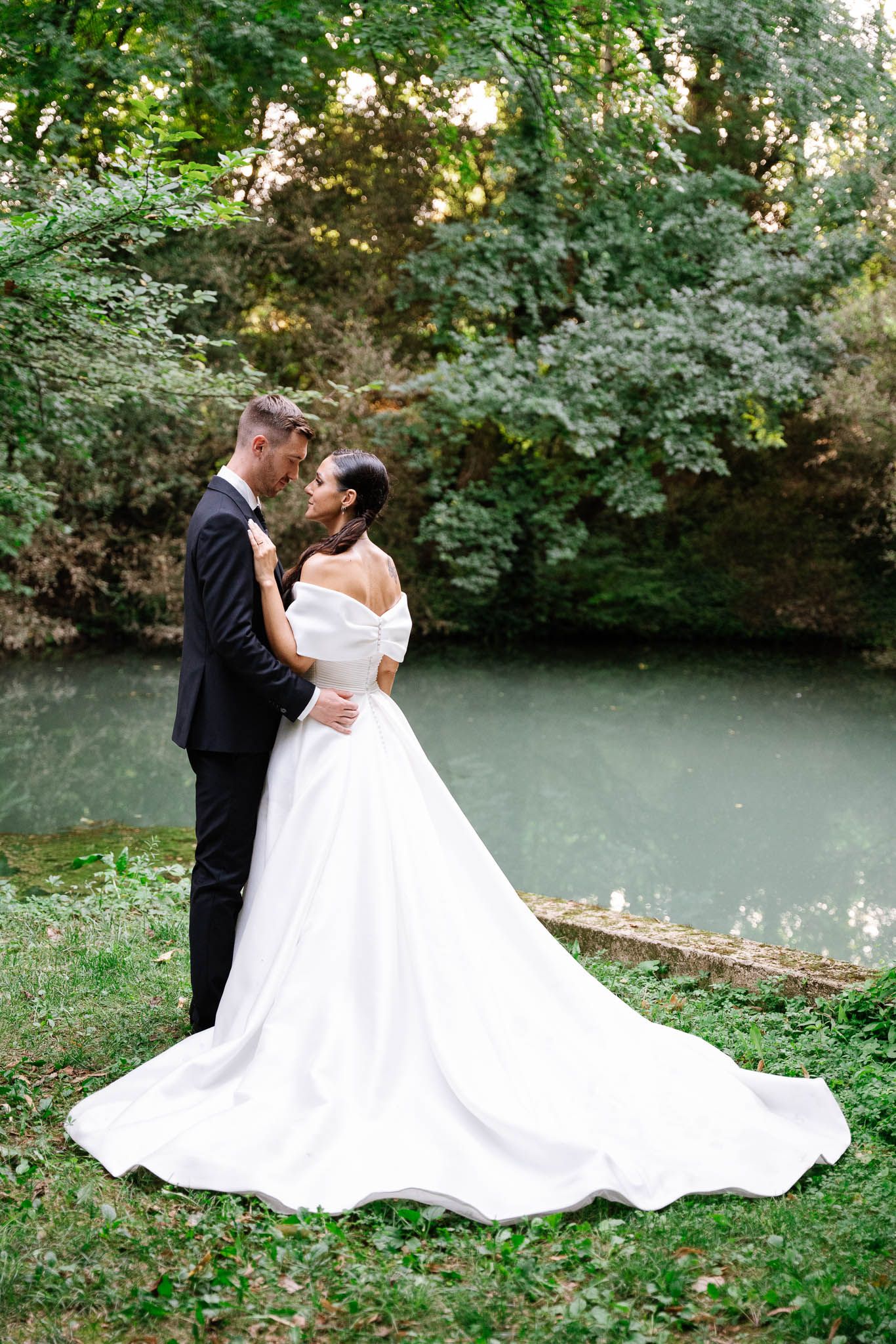 Newlyweds share romantic moments by a serene pond surrounded by lush greenery during their wedding photo session.
