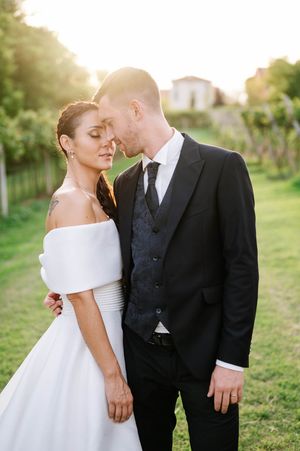 A couple shares intimate moments in formal wedding attire on a sunny lawn with greenery in the background.