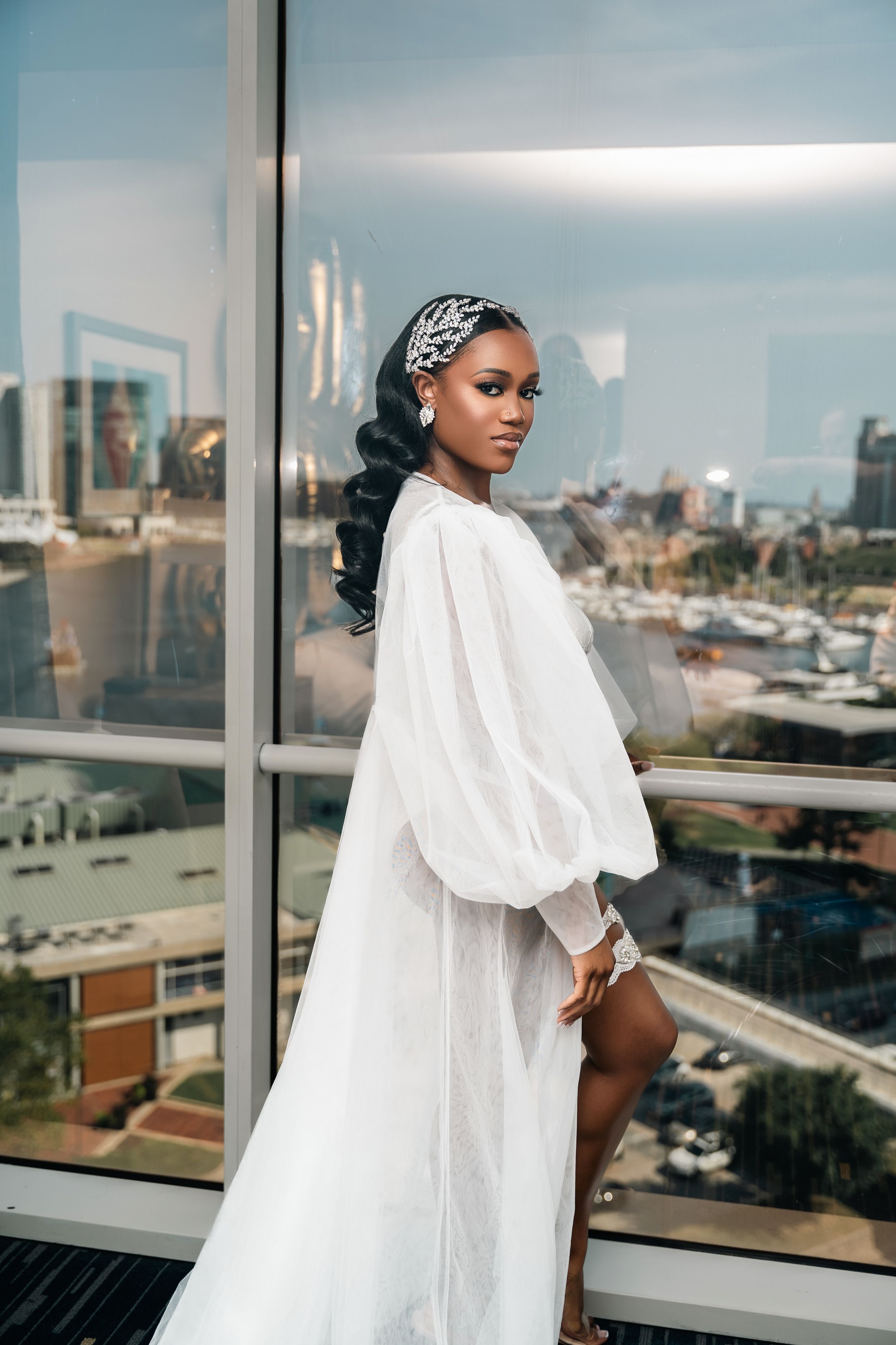 Elegant bridal portrait with flowing white robe against city view backdrop.