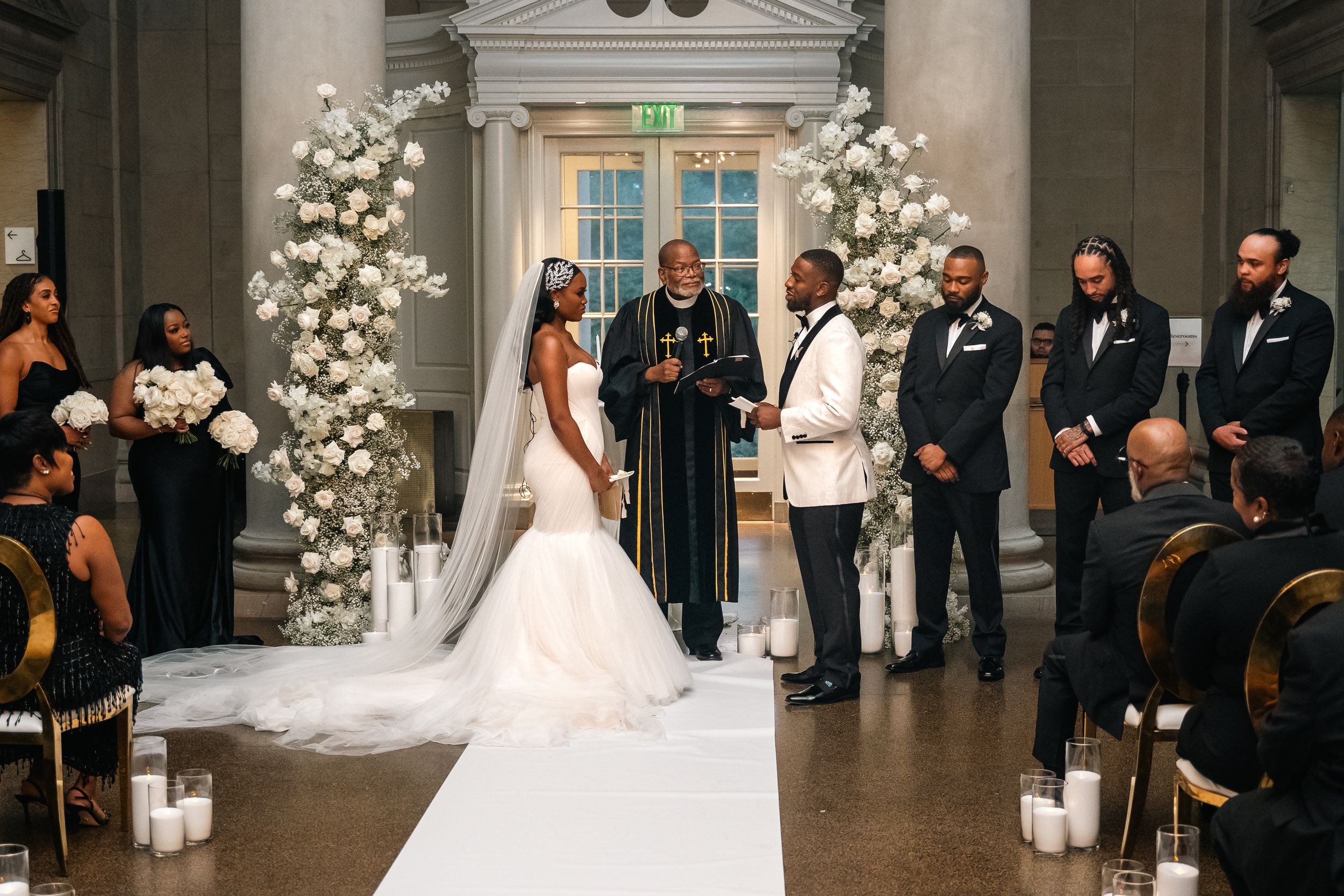 Wedding ceremony under ornate columns with floral arch and white aisle runner.