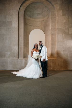 Elegant couple poses for wedding photo under stone archway in formal attire.