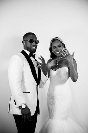 Black and white portrait of newlyweds showing off rings with joyful expressions.