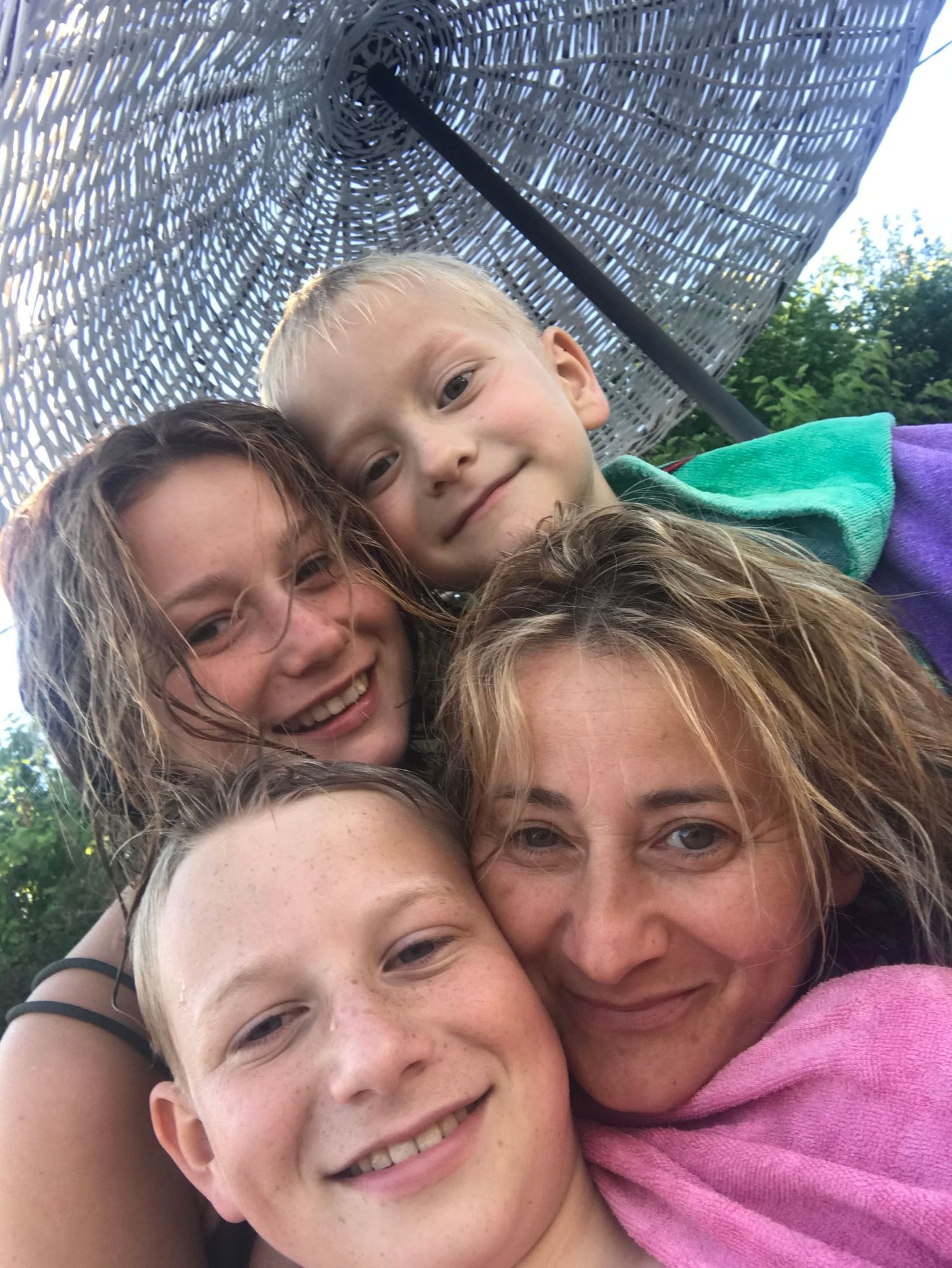 Close-up selfie of group huddled together under a gray umbrella.