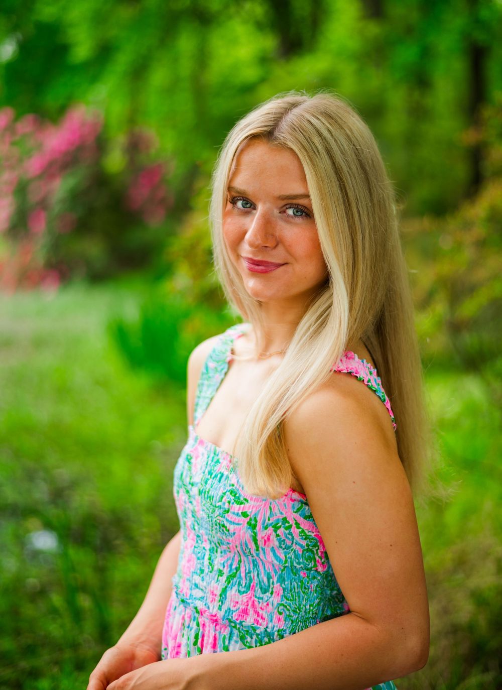A spring fashion portrait featuring a floral printed dress against a vibrant green garden background.