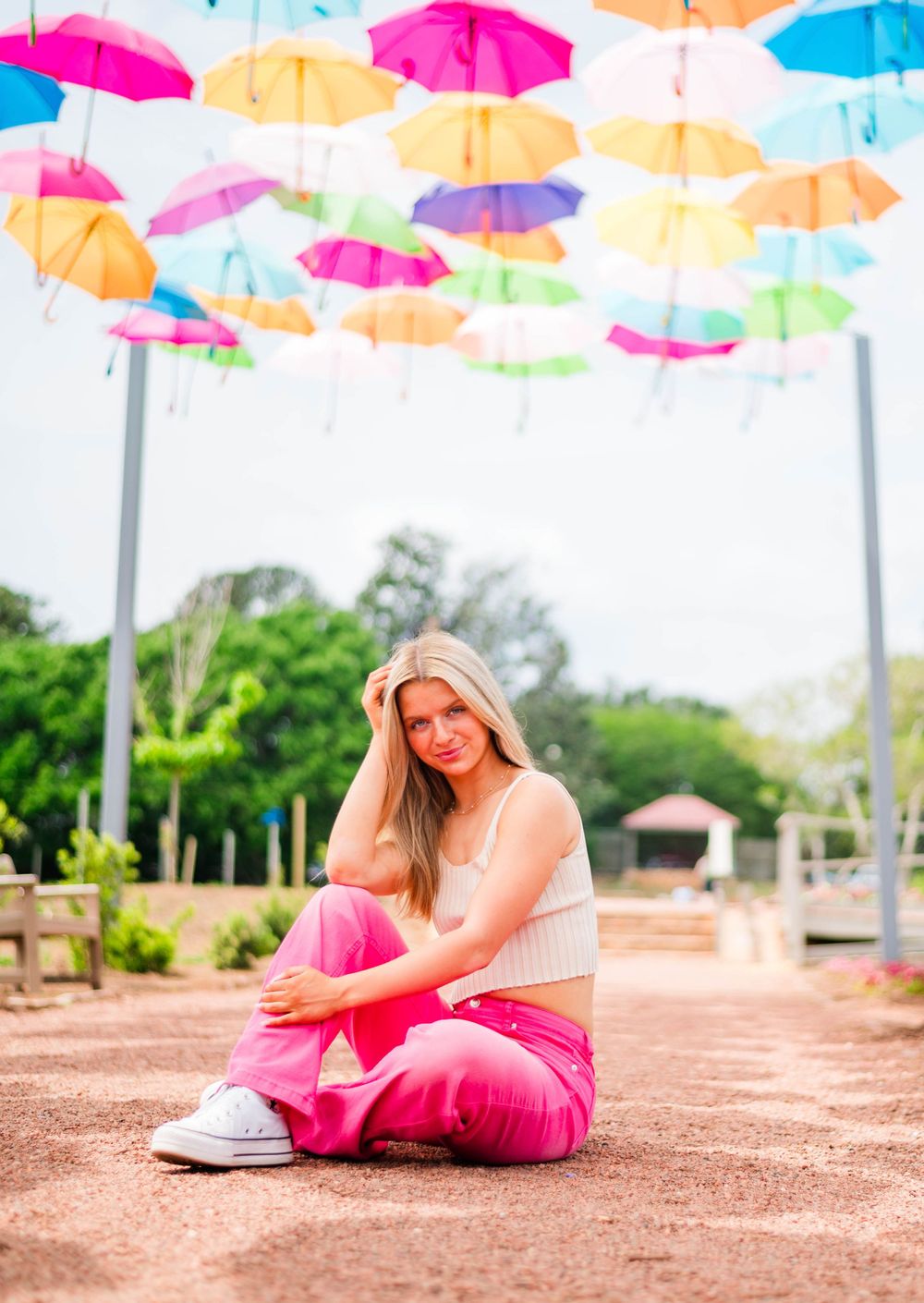 Relaxed outdoor portrait under vibrant umbrella installation wearing pink pants and cream top.