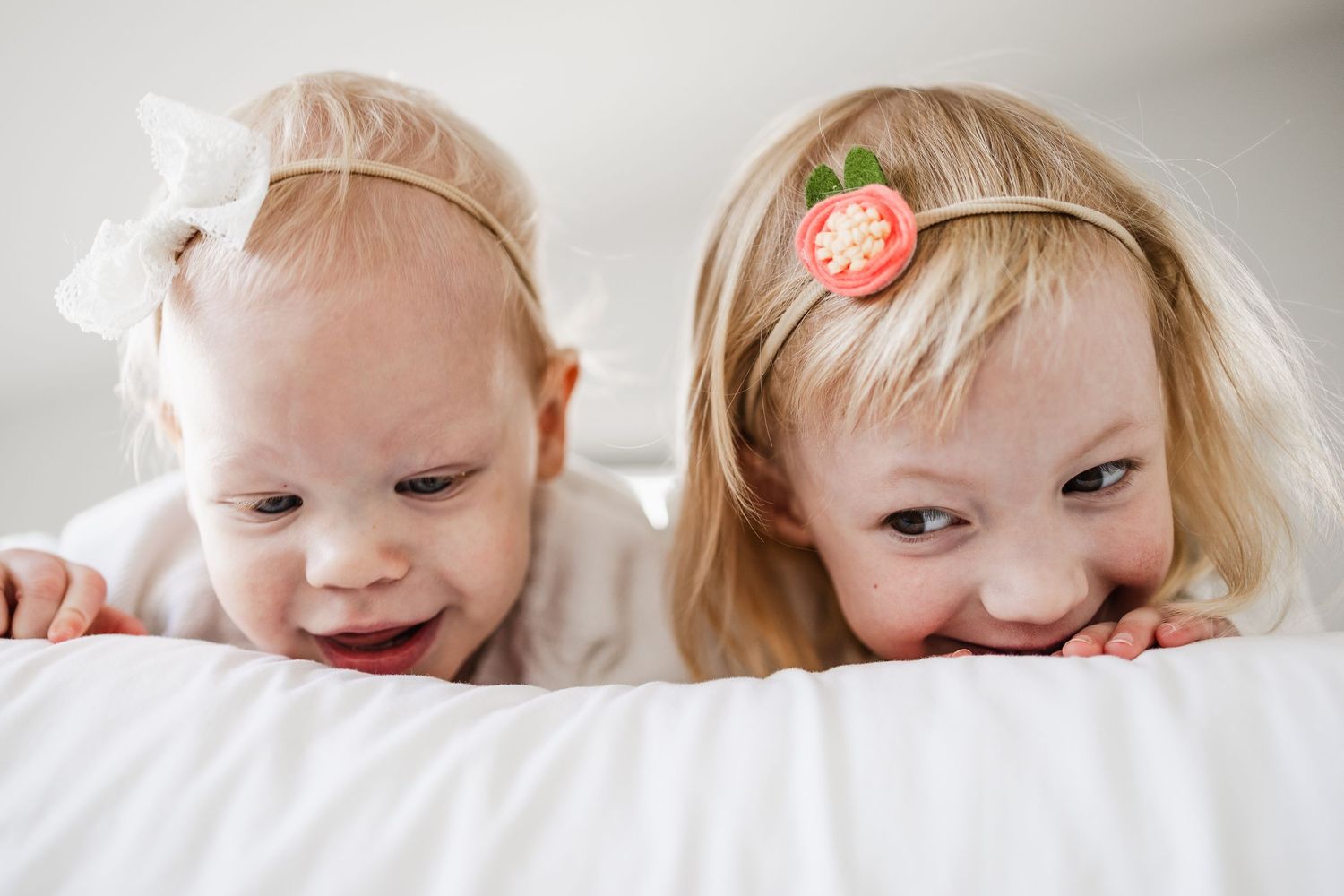 Two young girls peek over the edge of a bed