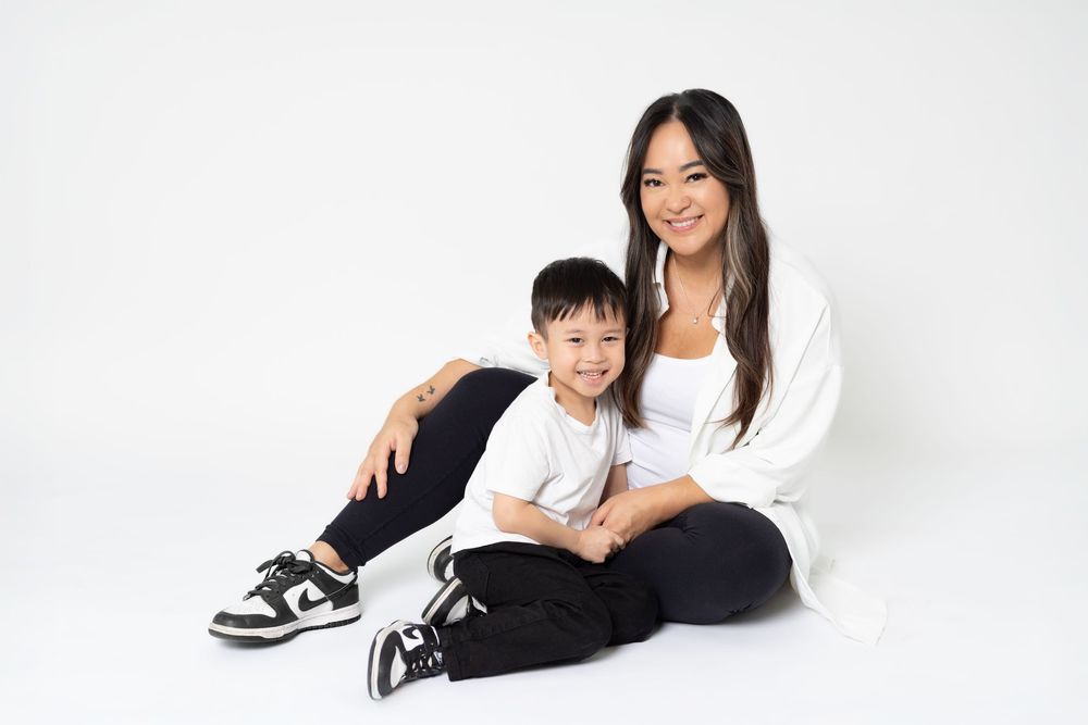 Two people in black and white outfits lounge casually on a white studio floor.