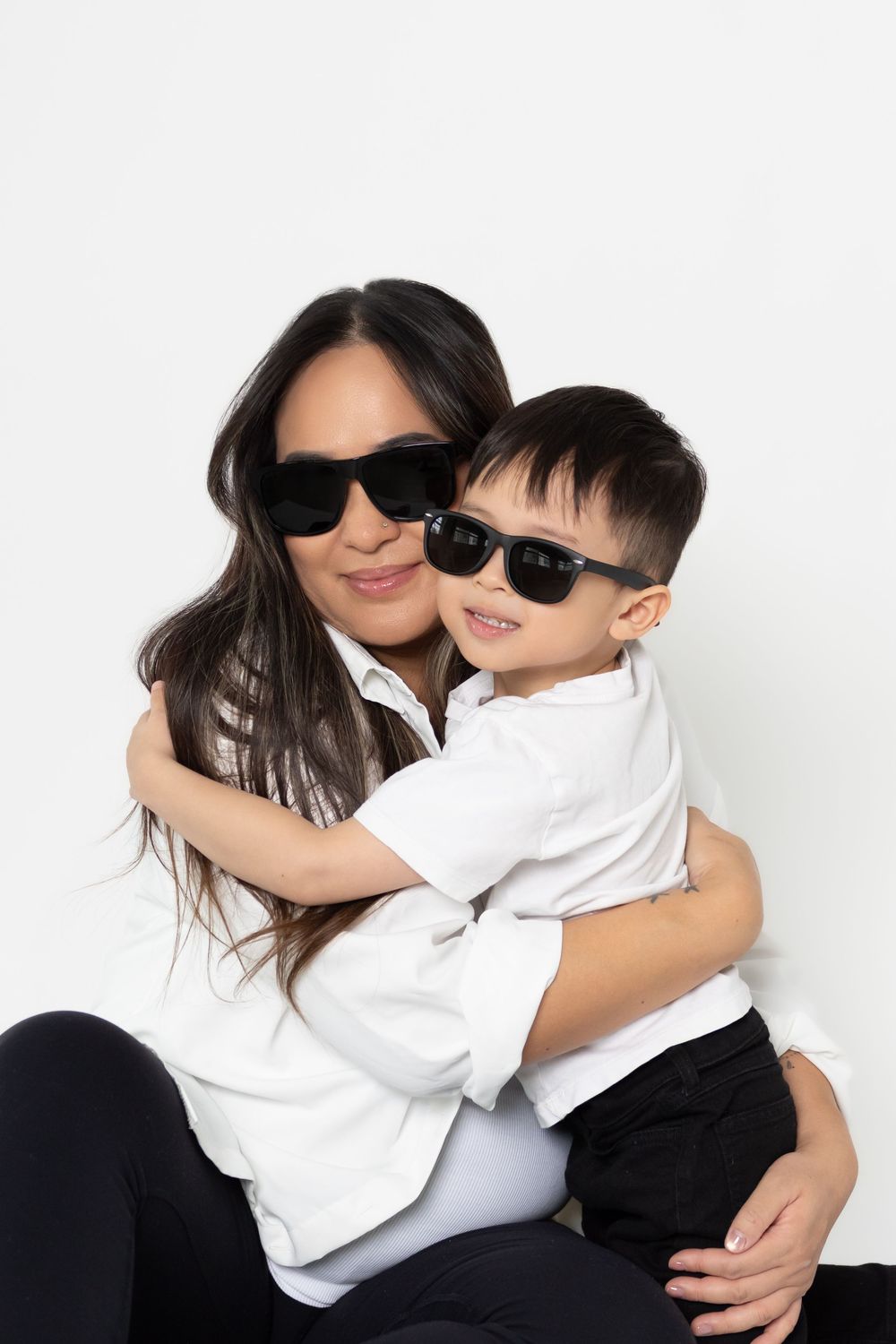 A stylish duo wearing sunglasses and matching white and black outfits pose playfully together in a photo series.