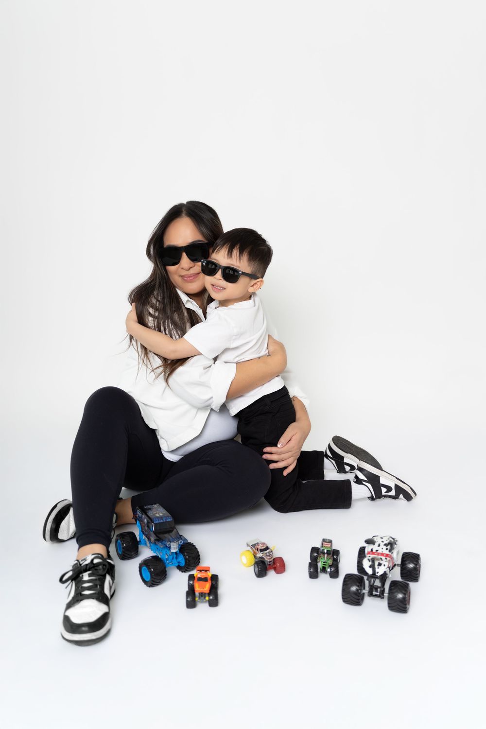 Parent and child playing with toy cars on white floor while wearing matching white shirts and black pants.
