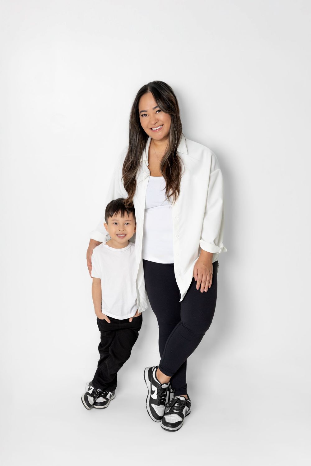 Two people wearing matching white tops and dark pants pose together against a white background.