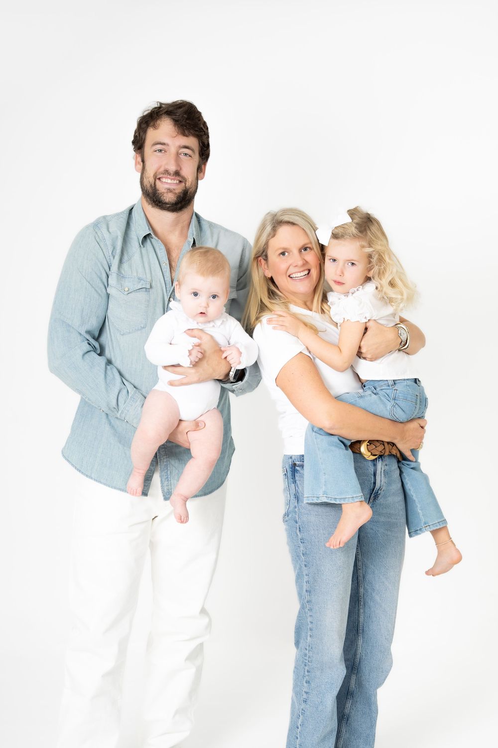 Family portrait against white background wearing casual denim and white outfits in studio setting.