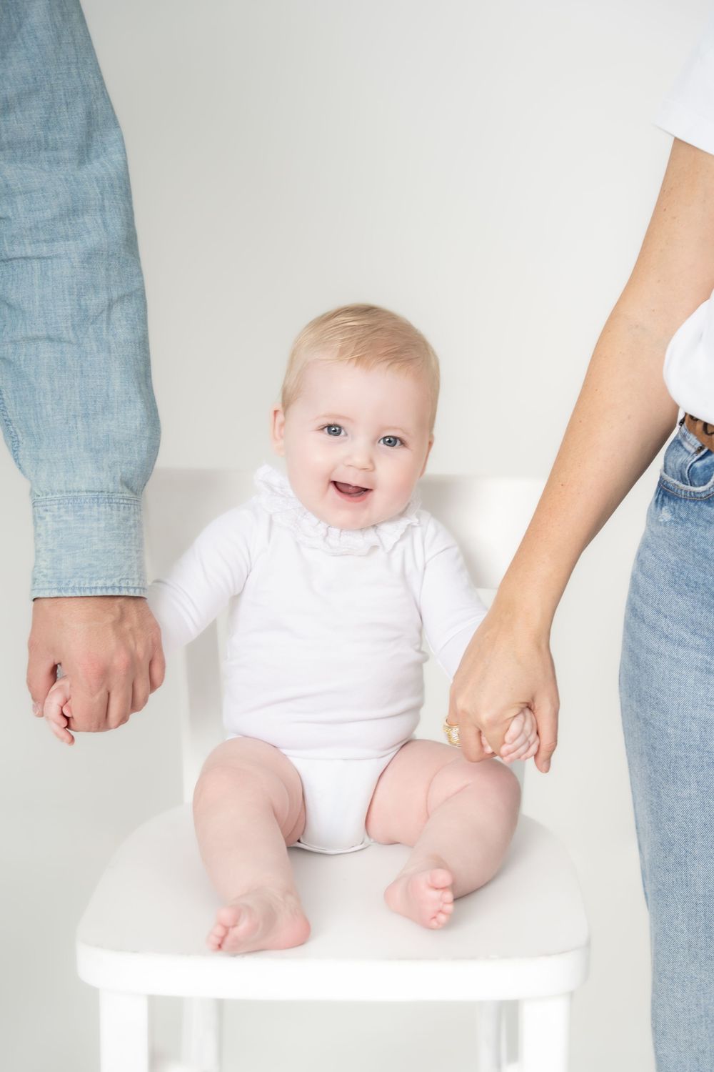 Baby in white onesie sitting on white surface with adult hands providing support shown in progression.