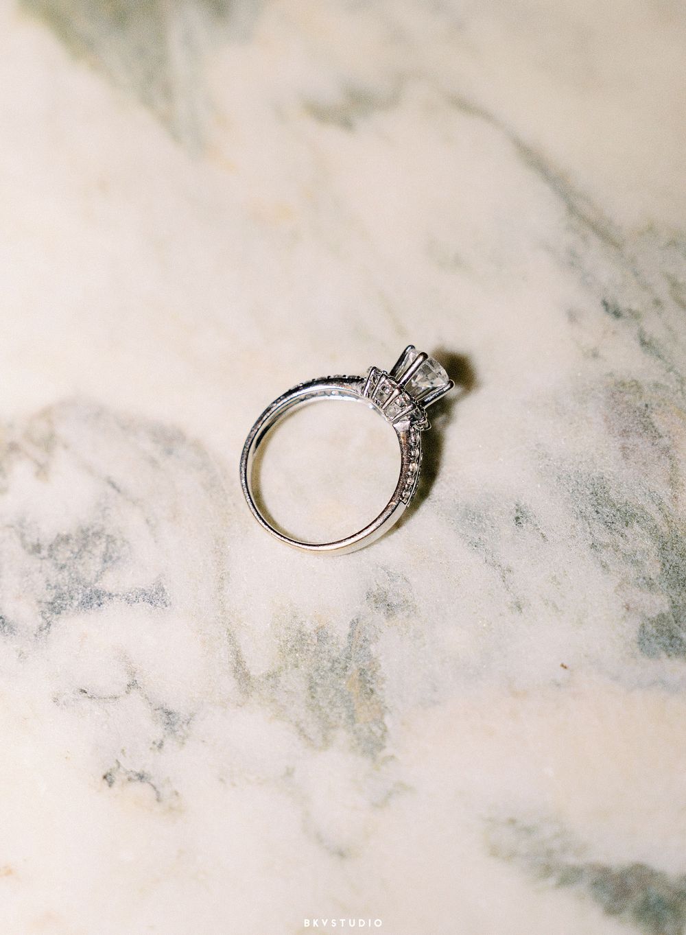 A sparkling diamond engagement ring with a delicate band rests on a luxurious white marble surface.
