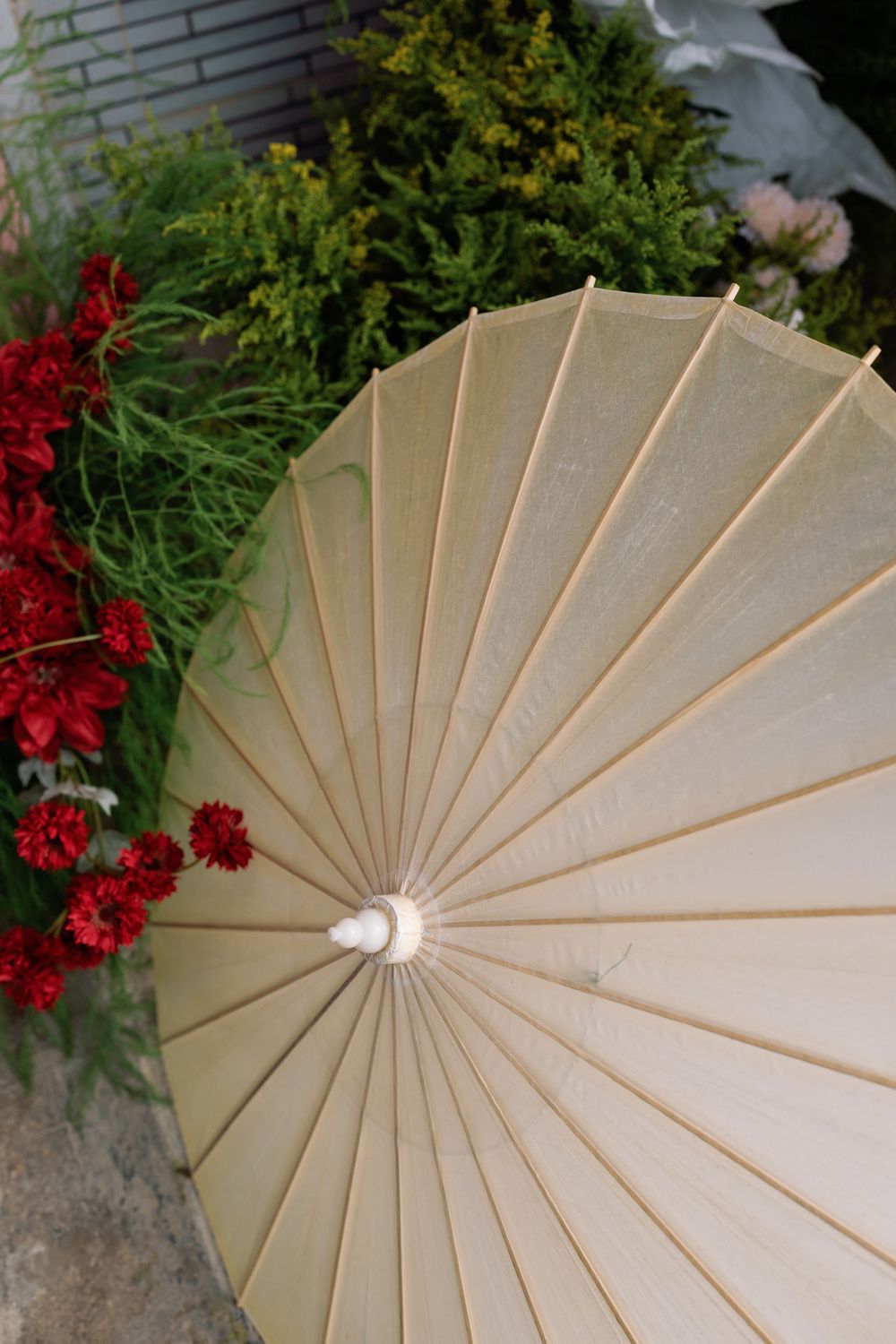 Beige paper parasol with bamboo ribs shown against red flowers and green foliage in garden setting.