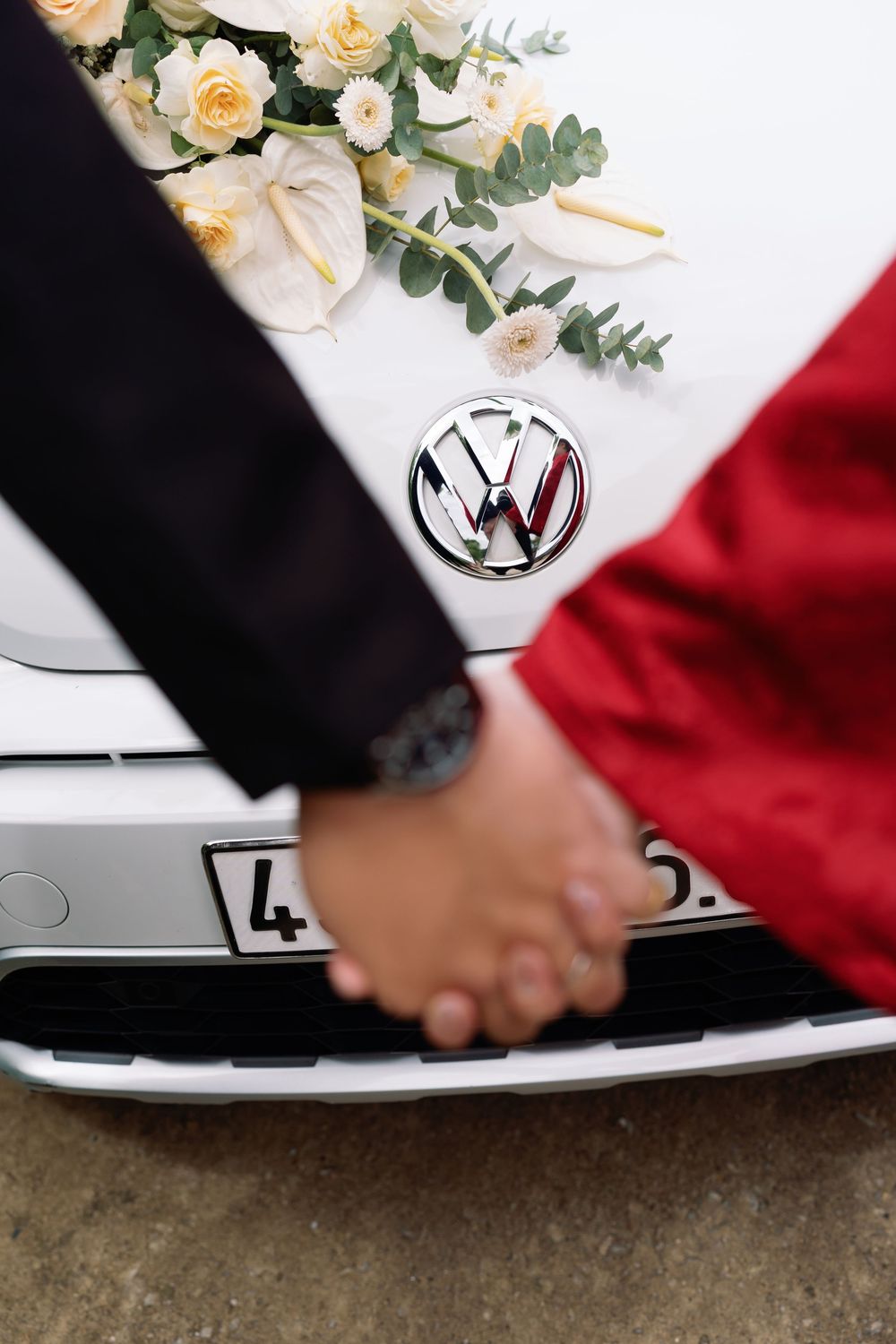 A close-up of clasped hands against a VW car logo with floral decorations and red and white fabric.