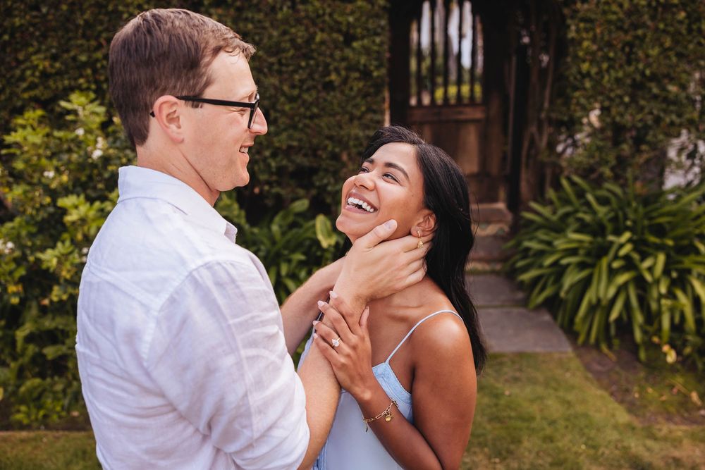 Happy interracial couple laughing together outdoors, man in white shirt and woman in blue sundress in garden.
