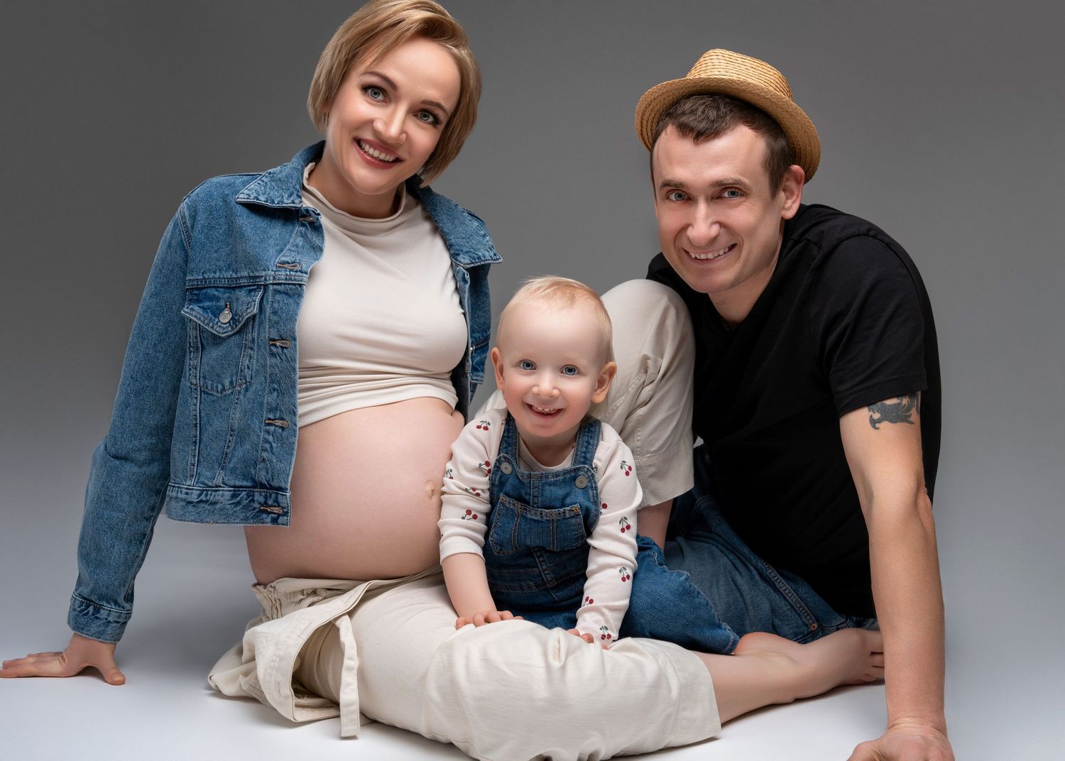 a woman wearing a crop top with her baby bump out sits in studio with her partner and toddler