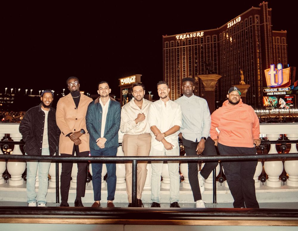 Group of seven men posing together outdoors on the Las Vegas Strip at night.
