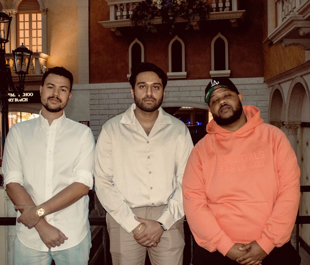 Three men pose together smiling inside The Venetian Las Vegas resort at night.