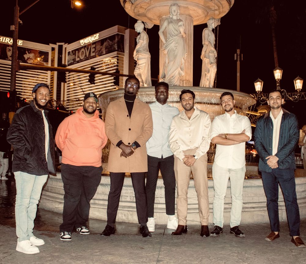 Group of seven men posing together near a fountain on the Las Vegas Strip at night.