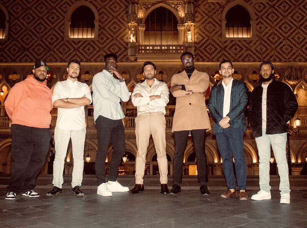 Group of seven men posing together inside an ornate golden architectural interior.
