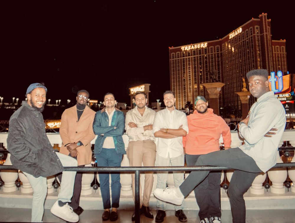 Group of seven men posing at night on Las Vegas Strip with Treasure Island hotel behind them.