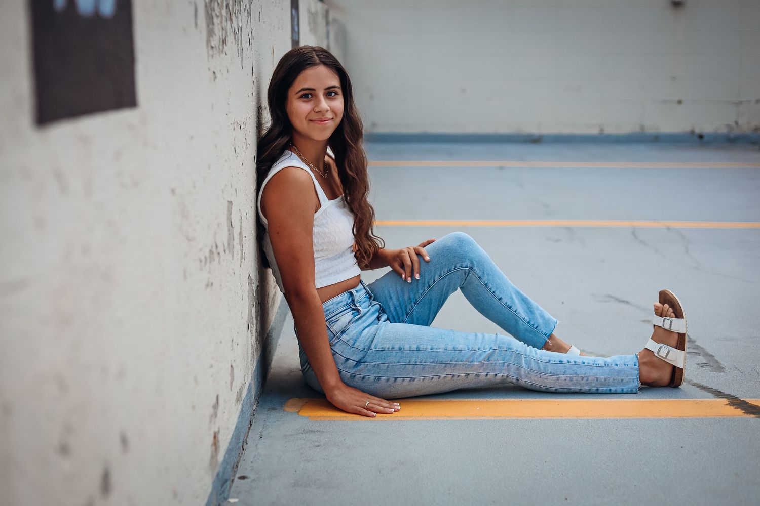 Woman in jeans and white top posing casually against a wall in an urban setting.