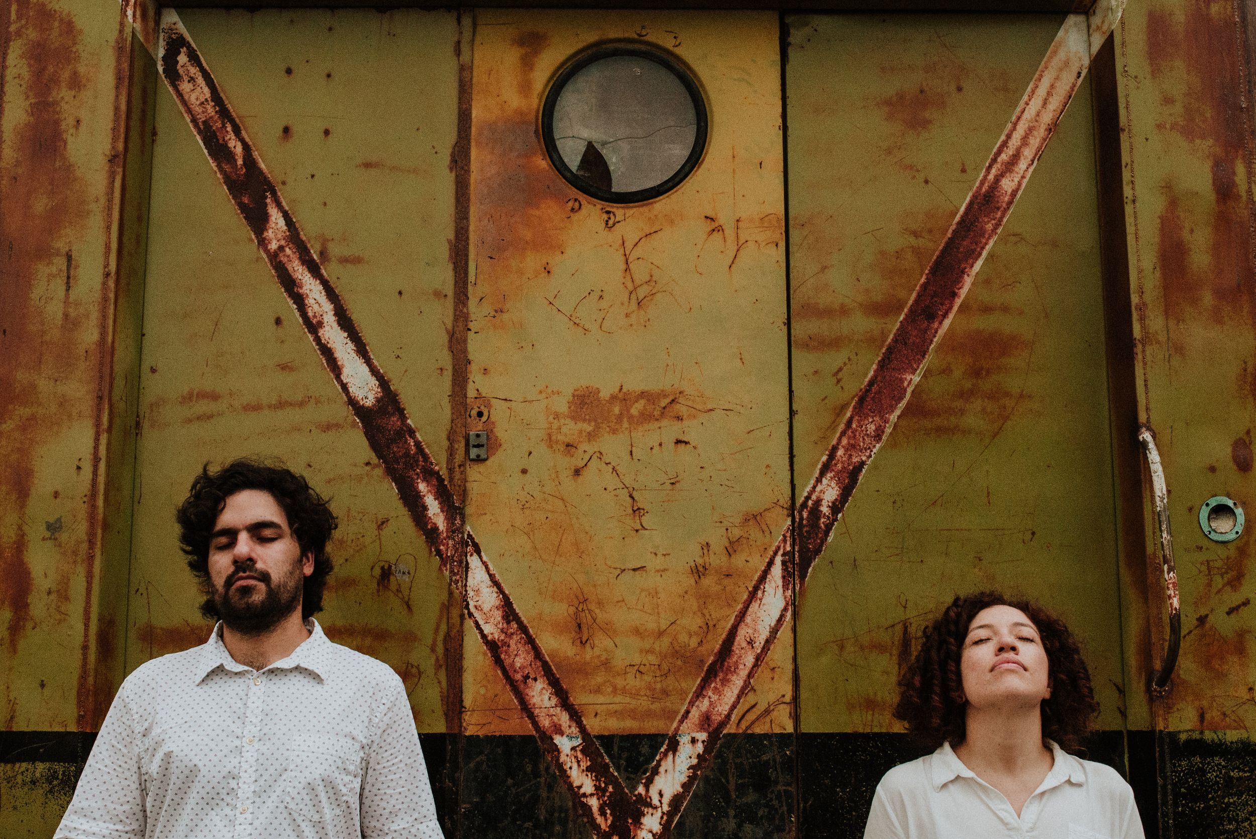 Couple standing apart in front of a rustic weathered yellow metal wall forming a V shape. Fotógrafo en Formosa