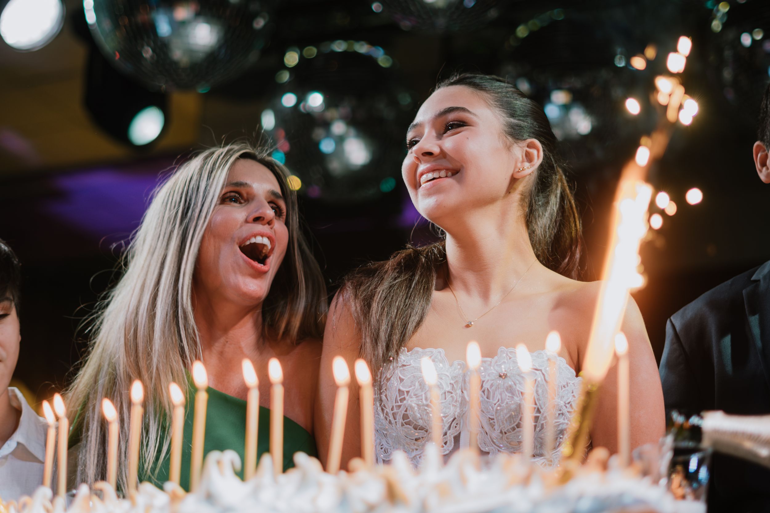 Two women laughing joyfully beside a birthday cake with lit candles and sparklers. Fotógrafo en Formosa