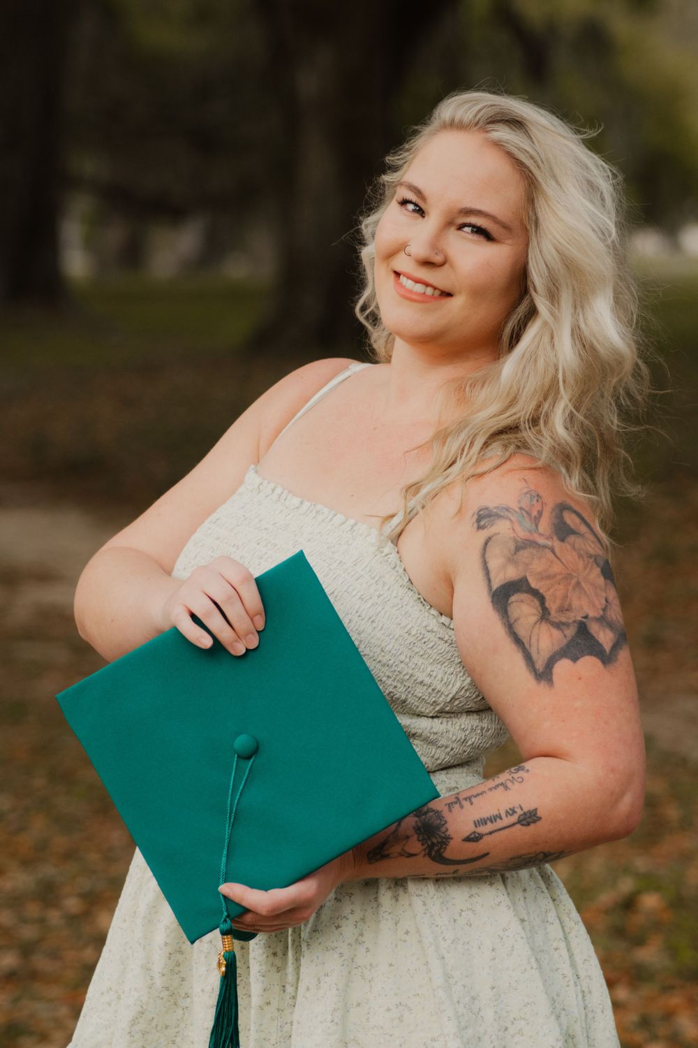 Graduate in emerald green cap and lace dress poses with graduation cap during spring graduation photoshoot.