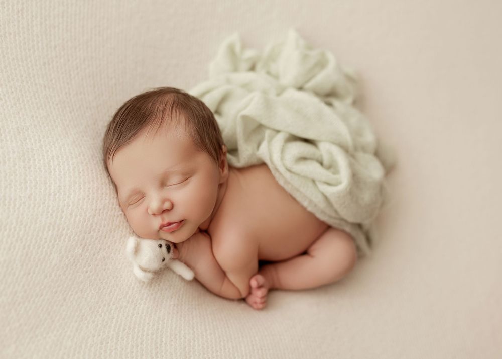 A sleeping newborn baby lies peacefully on soft cream-colored fabric with a delicate bow headband.