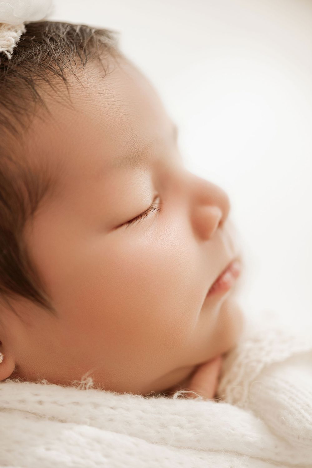 A sleeping newborn baby rests peacefully on soft white fabric in a gentle sepia-toned photograph.