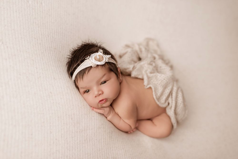 A sleeping newborn baby wrapped in cream-colored fabric rests peacefully in a minimalist photography setting.