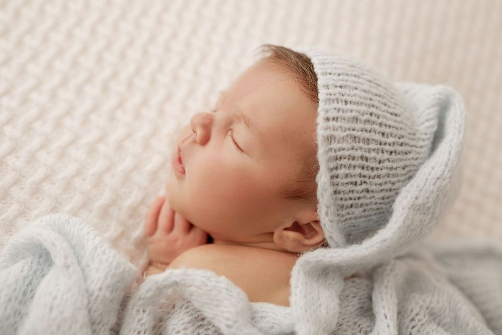 Newborn baby sleeping peacefully in soft white bedding while wearing a cozy gray knit hat.