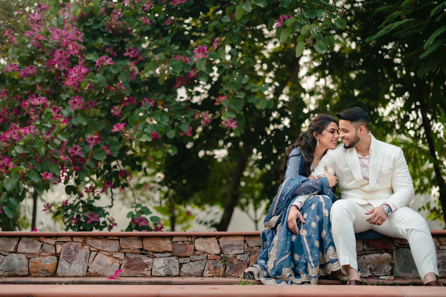 Couple relaxing on stone wall surrounded by blooming pink and white flowers.