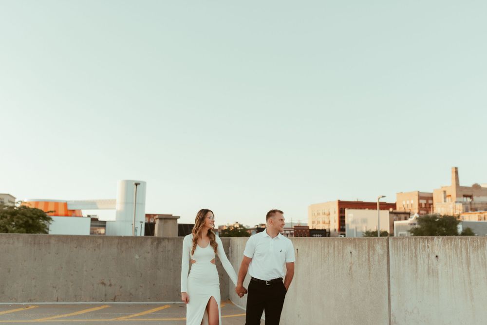 Couple holding hands while walking on urban rooftop at sunset.