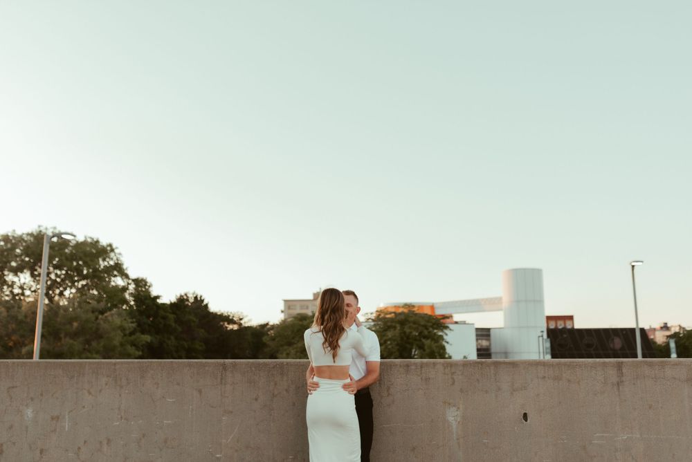 Couple sharing intimate moment against concrete wall with city skyline in background.