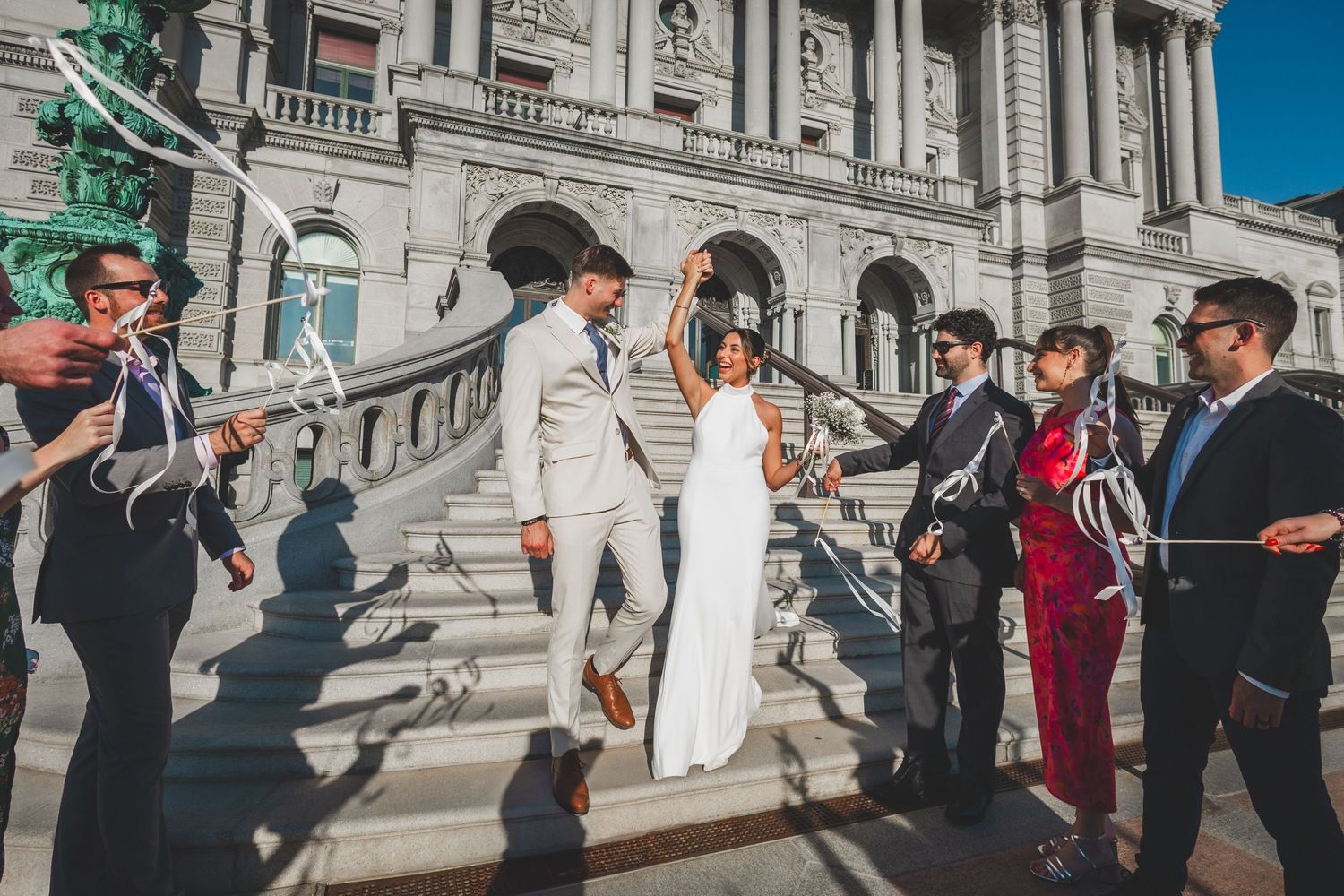 Wedding party descends grand stone steps of historic government building.