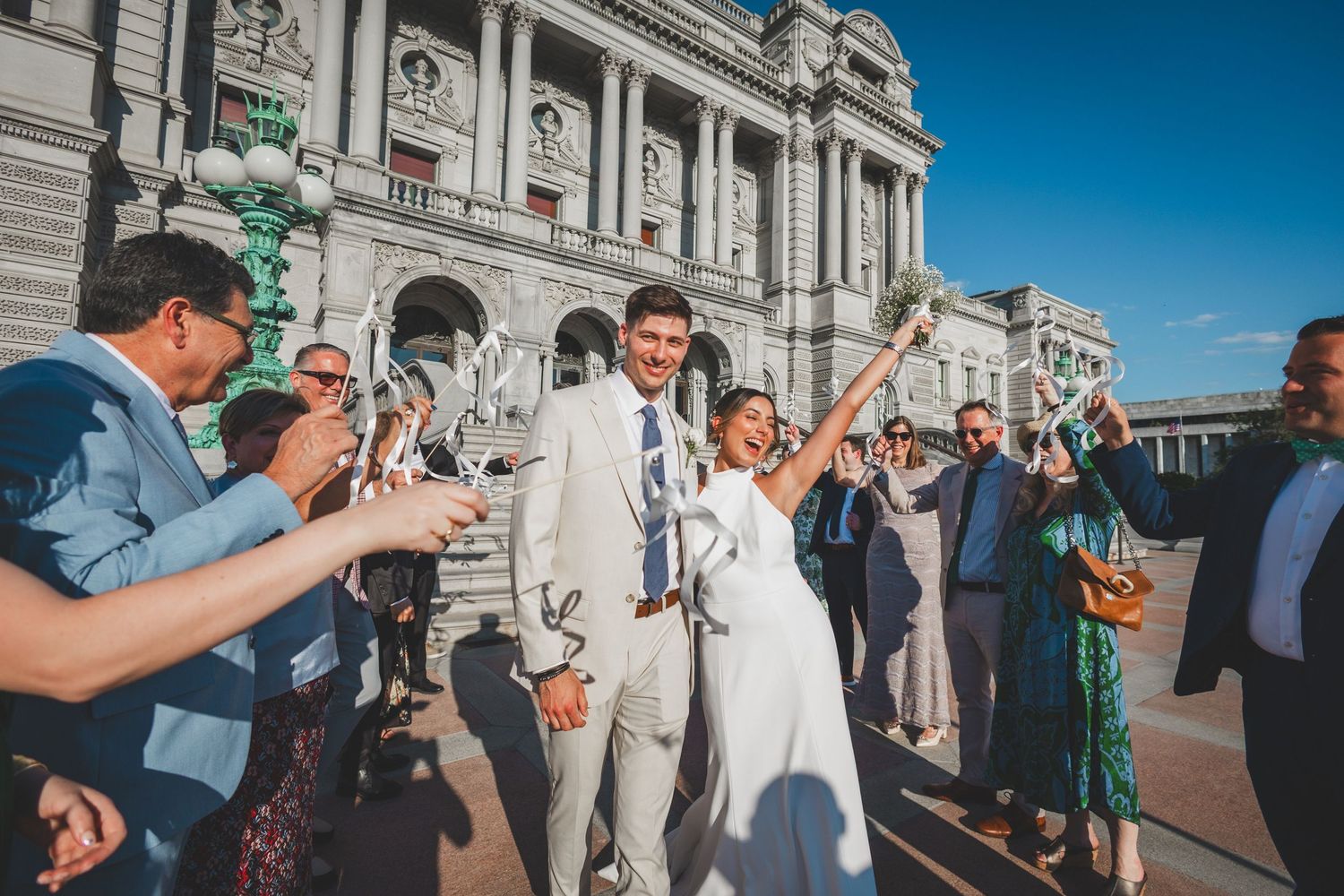 Wedding party celebrating with bubbles on marble steps of neoclassical building.