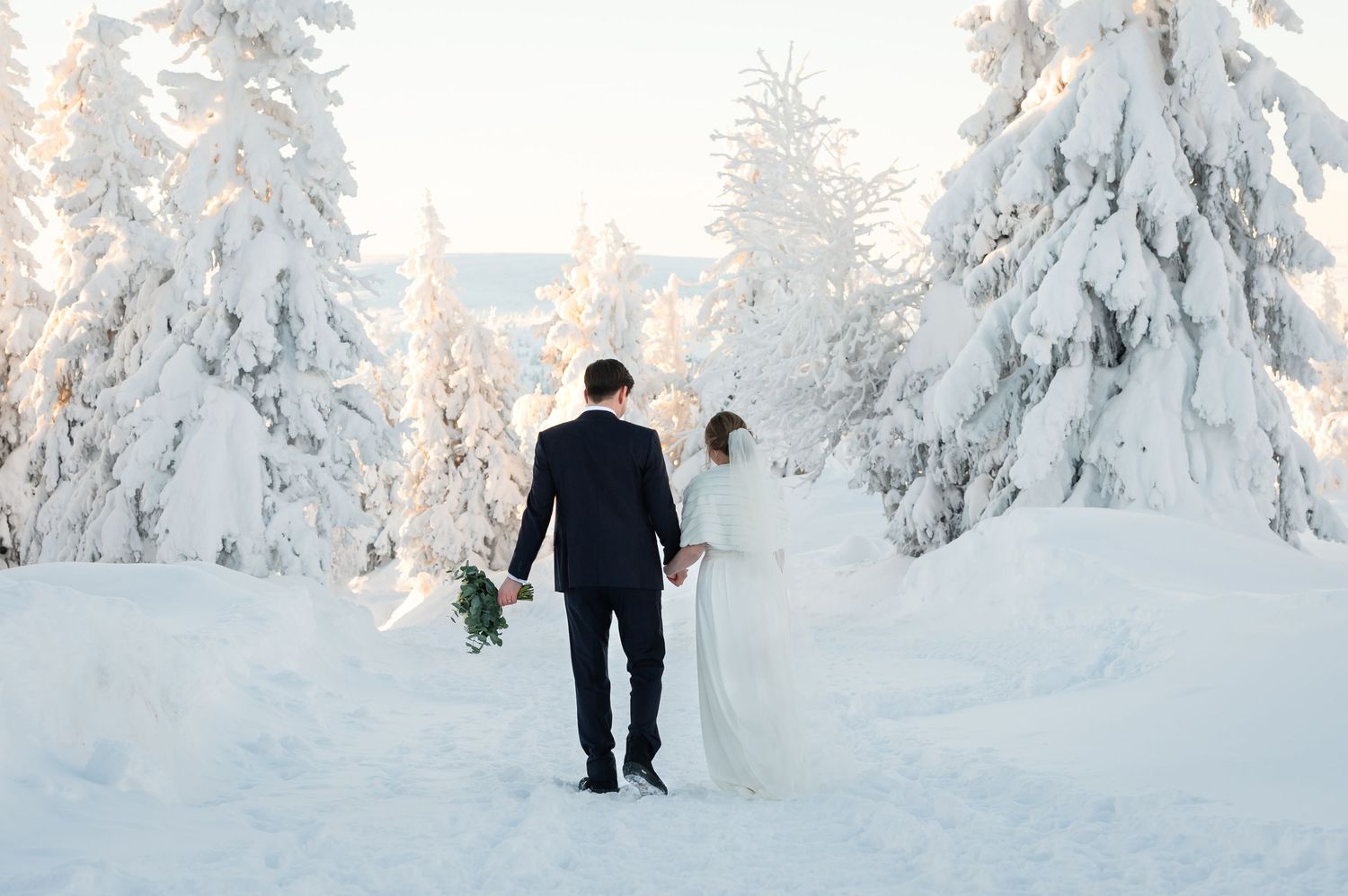 Brudpar går bort ifrån kameran på snötäckt väg och håller handen.