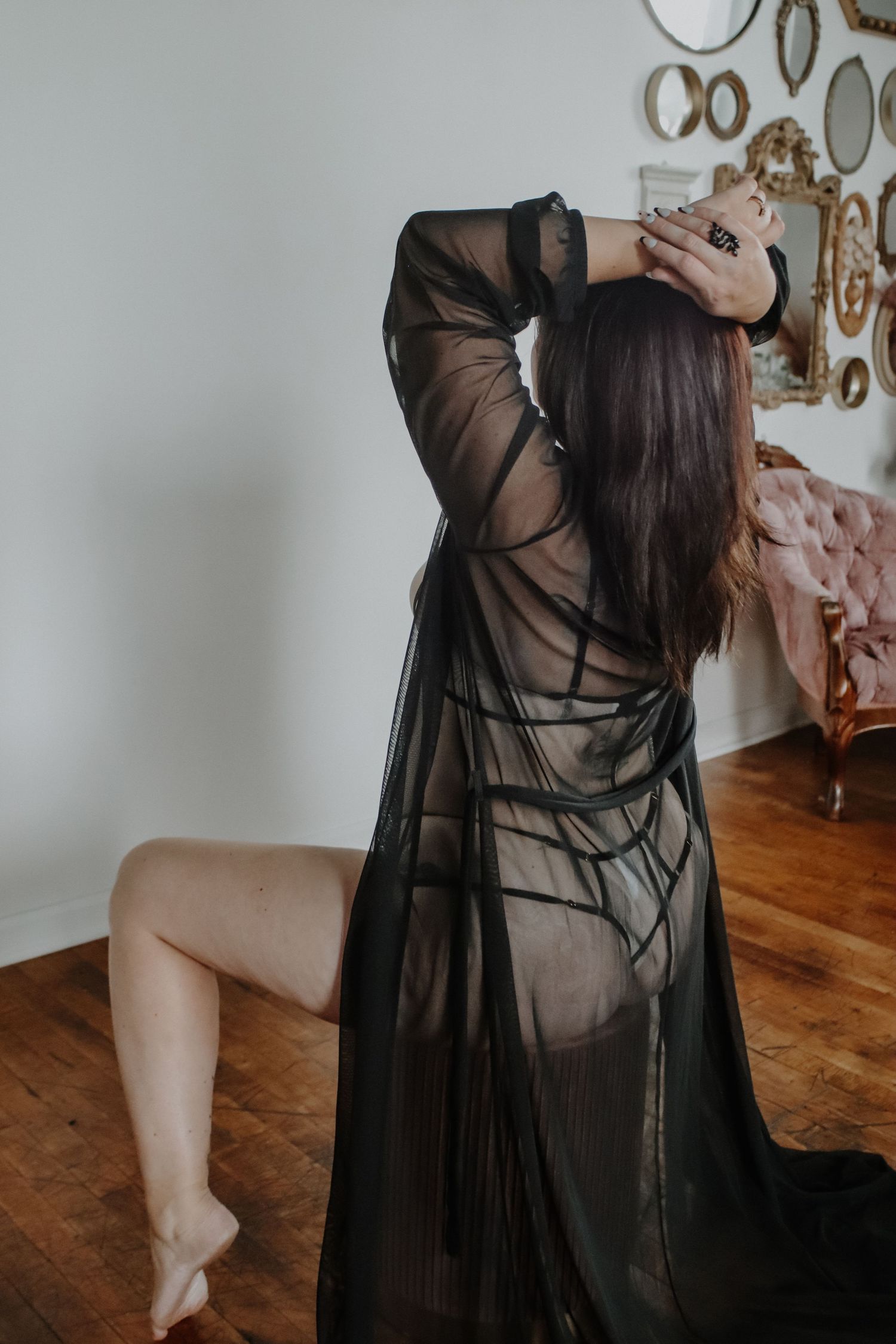 Woman in sheer black robe poses artistically in room with decorative wall mirrors.