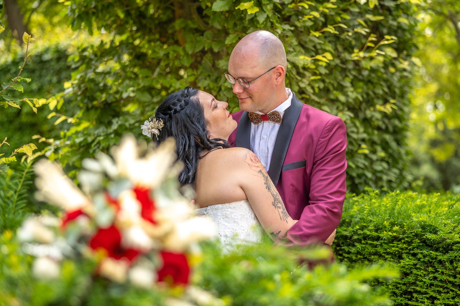A romantic wedding portrait in a lush garden setting with red florals.