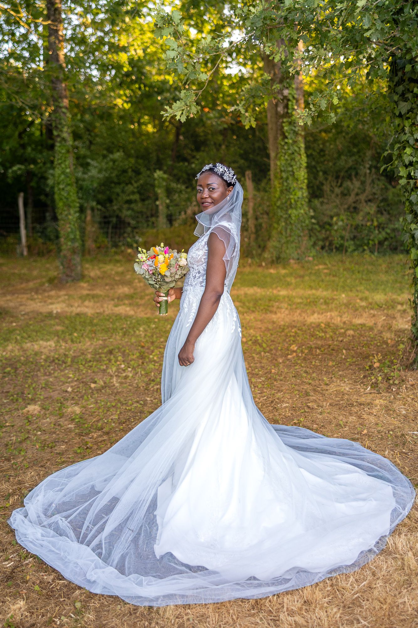 Elegant bridal portrait showcasing flowing white wedding gown with cathedral train in woodland setting.