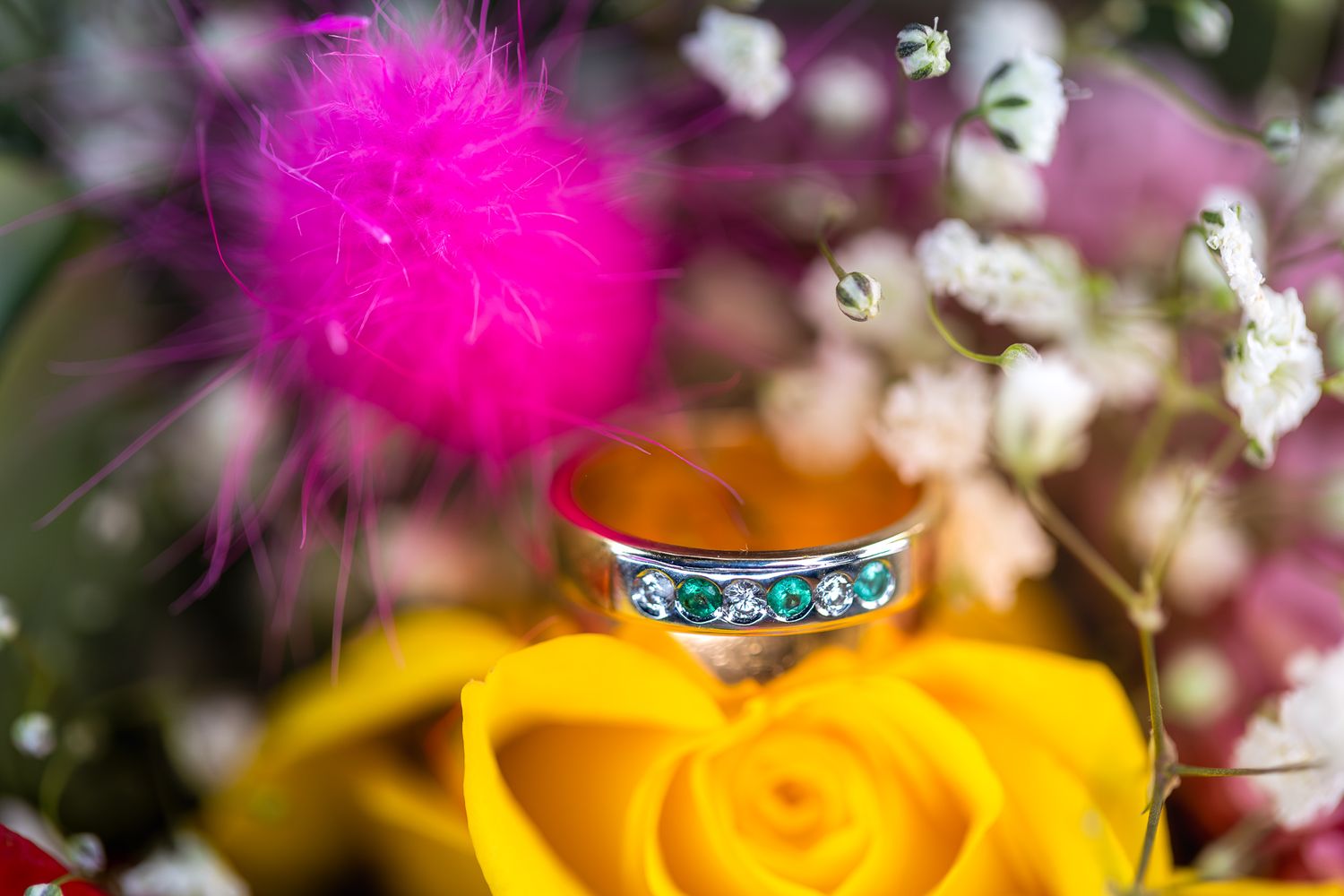 Wedding rings displayed among pink and yellow flowers with sparkling details.