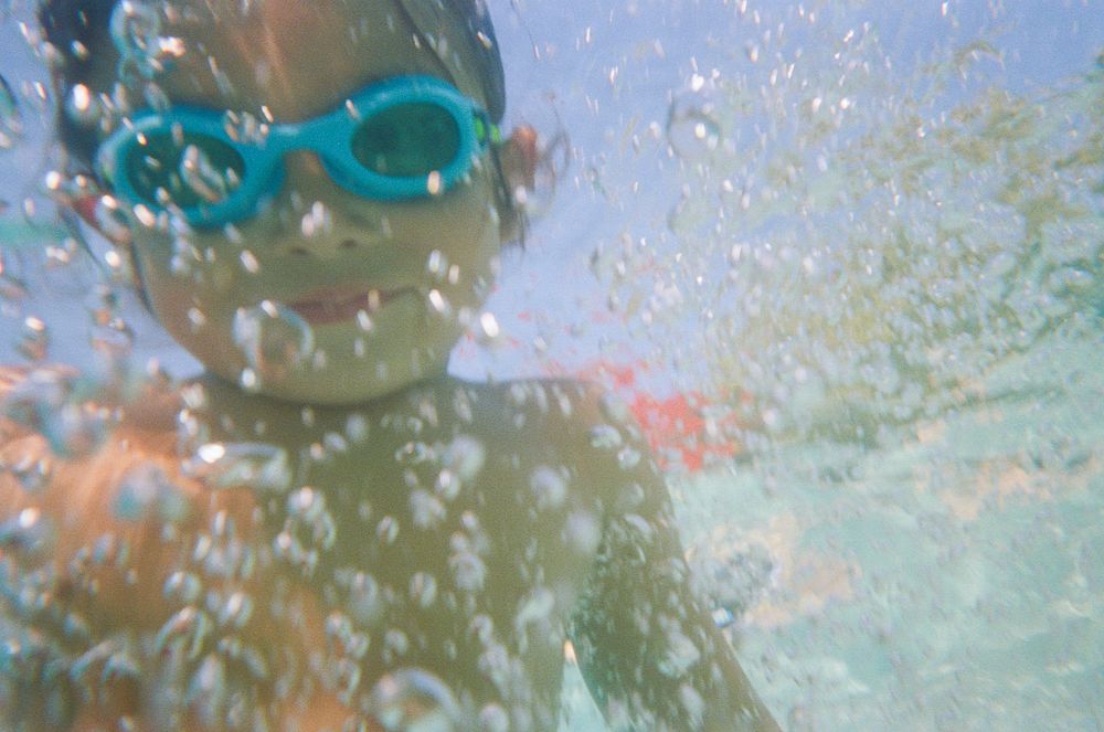 Blurry underwater selfie of a swimmer wearing teal goggles surrounded by bubbles.