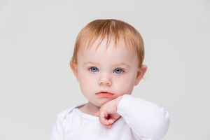 A toddler in a white shirt sticks their tongue out playfully while looking at the camera.