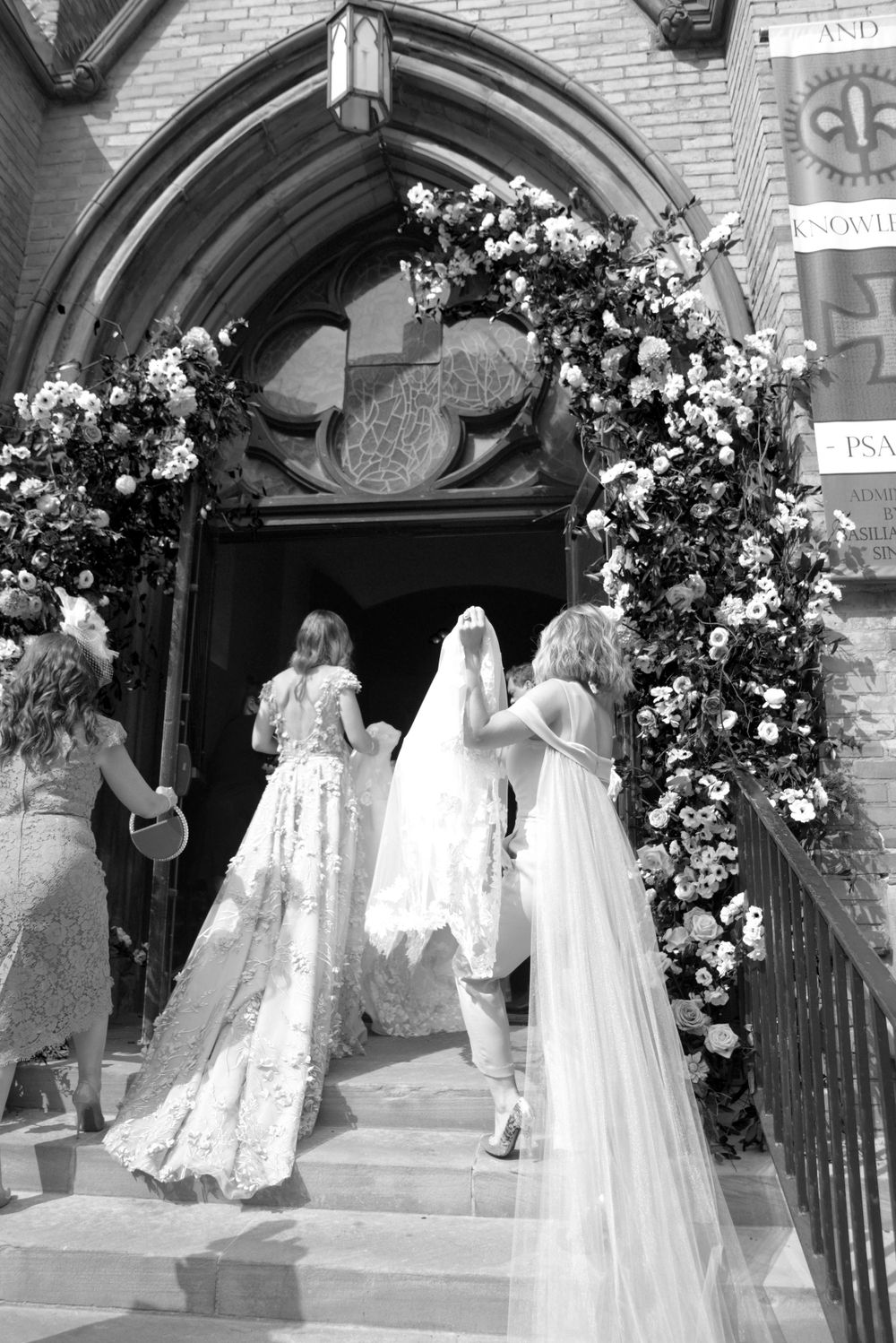 A wedding party enters a church through an archway decorated with floral arrangements.