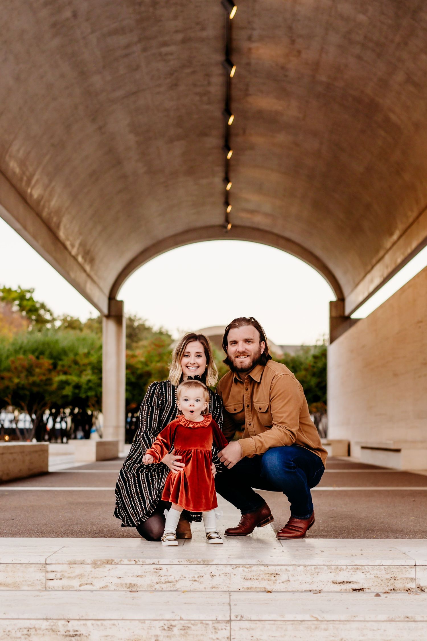 Family poses together under concrete archway with warm lighting and architectural details.