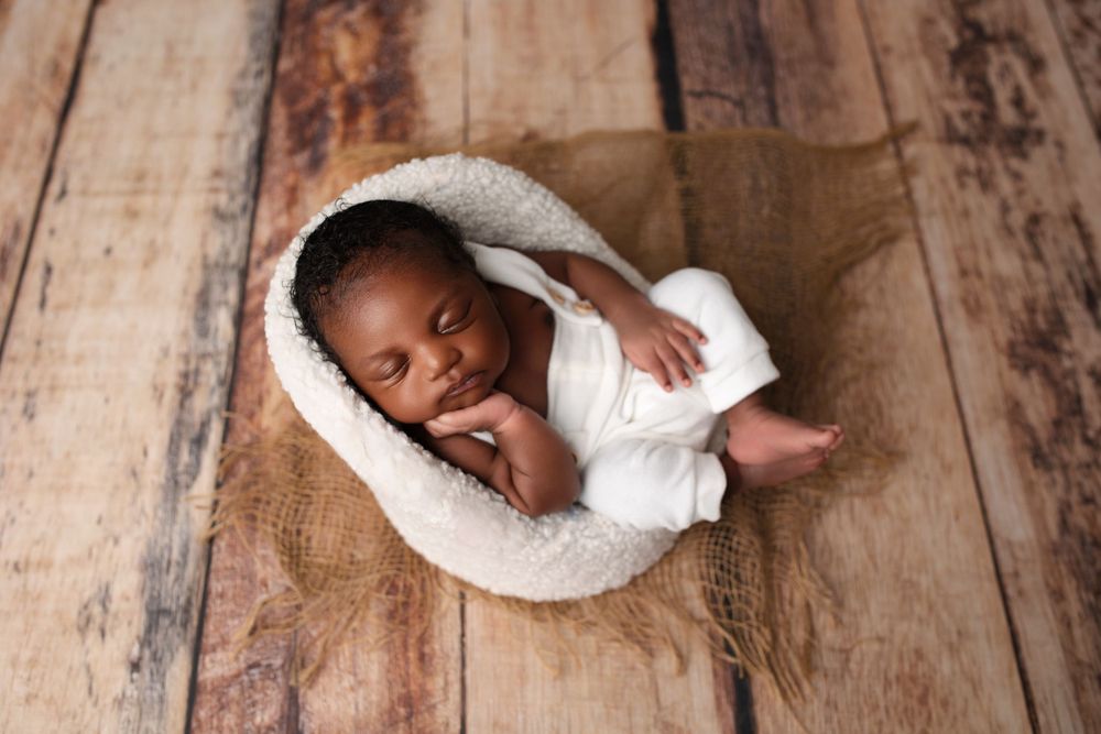 Peaceful sleeping newborn in white wrap nestled in cozy cream-colored basket on wooden floor.