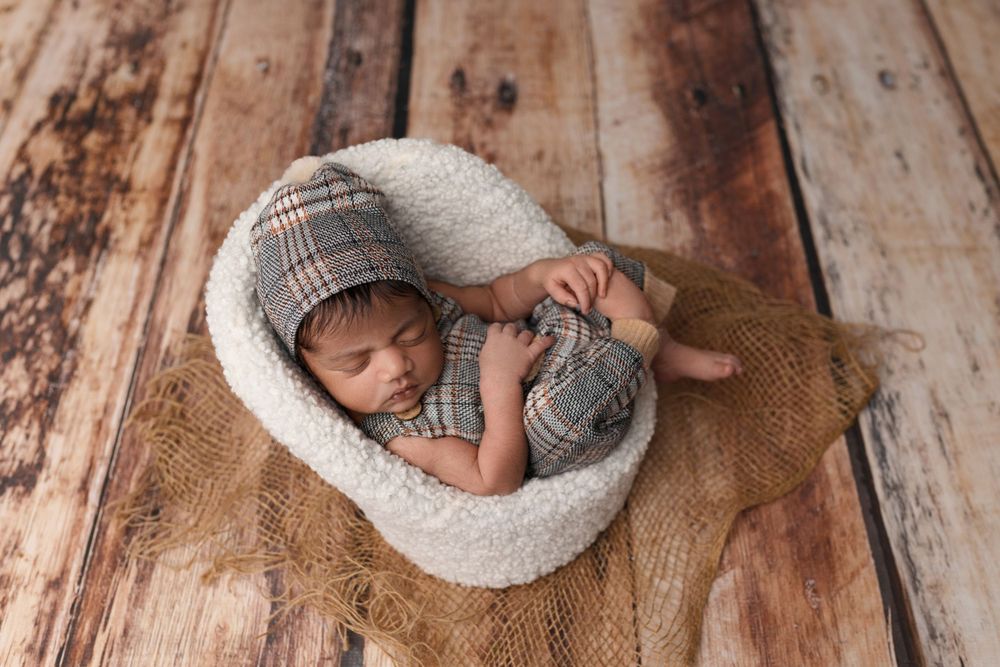 Sleeping newborn wrapped in grey knit blanket on wooden floor backdrop.